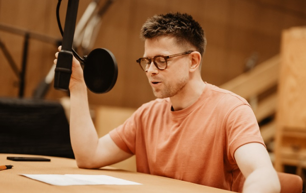 Na zdjęciu aktor Paweł Krucz czytający tekst do mikrofonu w studiu nagrań